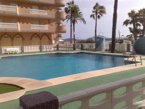 a swimming pool in front of a building with palm trees at Ático Castillo de Mar in La Manga del Mar Menor