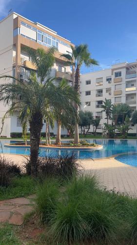 a building with palm trees in front of a swimming pool at Galia Mohammedia residence POOL WIFI in Mohammedia