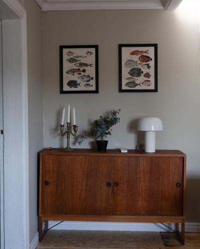 a room with a wooden cabinet with a lamp and two pictures at Lovely cabin with a beautiful view over Byske river in Byske