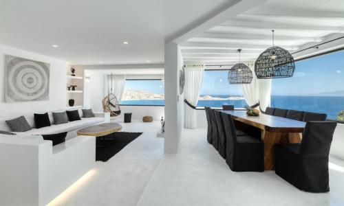 ein Wohnzimmer mit einem Tisch, Stühlen und Meerblick in der Unterkunft Mbc Psarou Black Retreat 11 Bedrooms Mykonos in Psarrou