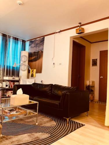 a living room with a black leather couch and a glass table at Stay Banwoldang in Daegu
