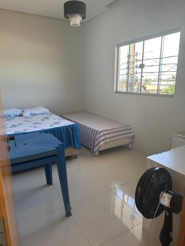 a room with two beds and a table and a window at Apartamento da Pâm - em frente ao clube cantão in Pontes e Lacerda