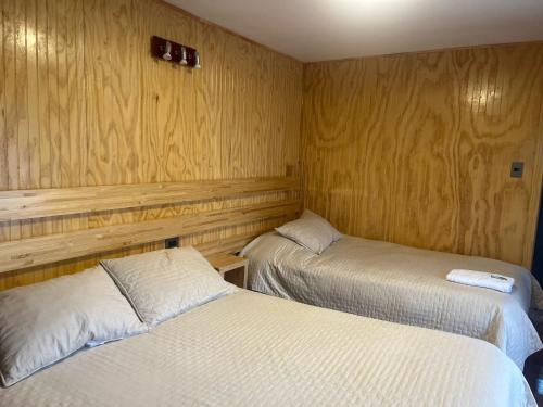 two beds in a room with wooden walls at Hostal Español Coyhaique in Coihaique