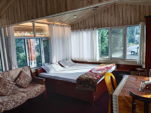 a bedroom with a bed and two chairs and windows at Gulab - B Homestay in Dehradun