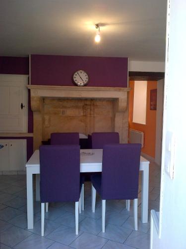stół z fioletowymi krzesłami i zegar na kominku w obiekcie Maison Individuelle Les Templiers w mieście Bure-les-Templiers