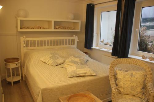 ein Schlafzimmer mit einem Bett und einem Stuhl sowie zwei Fenstern in der Unterkunft Reetdach Friesenhof Süderende in Westerland