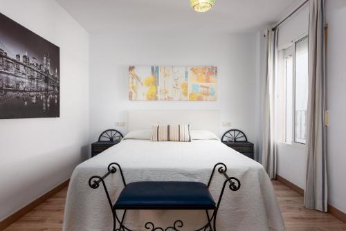 a white bedroom with a bed with a blue chair at Manilva Home in San Luis de Sabinillas