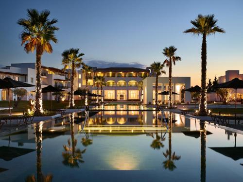 um resort com piscina e palmeiras à noite em Casa Marron Grecotel All Inclusive Resort em Kalamákion