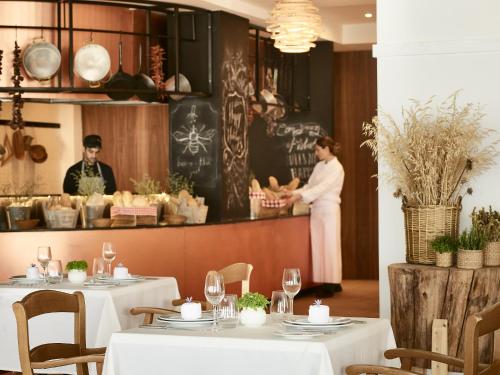 Un restaurante con mesas blancas y una mujer parada en el mostrador. en Grecotel Casa Marron, en Kalamákion