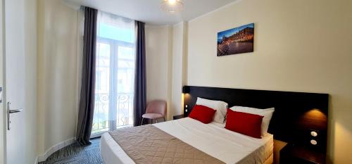 Un dormitorio con una cama con almohadas rojas y una ventana en Evelia Hotels, en Niza