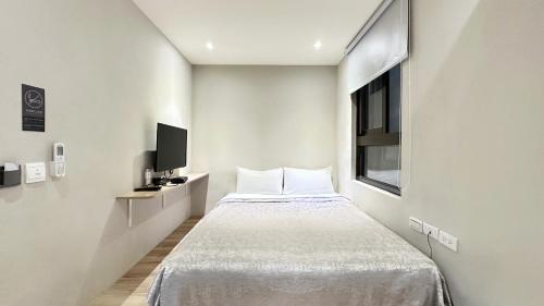 a small white bedroom with a bed and a window at WE Hotel in Miaoli