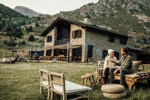 two people sitting on a bench in front of a house at L´Ovella Negra Mountain Lodge in Canillo