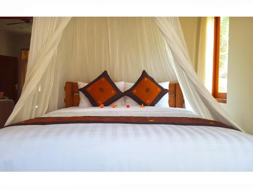 a white bed with orange pillows and a canopy at Juada Garden in Seminyak
