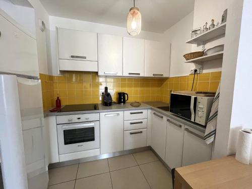 une cuisine avec des placards blancs et du carrelage jaune dans l'établissement MORIANI Plage T2 terrasse proche mer et commerces, à Moriani-Plage