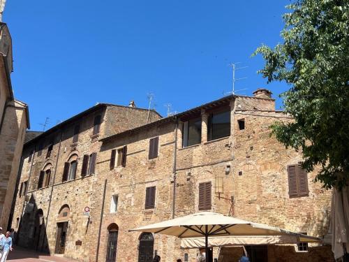 - un grand bâtiment en briques avec un parasol devant dans l'établissement A La Casa Dei Potenti, à San Gimignano
