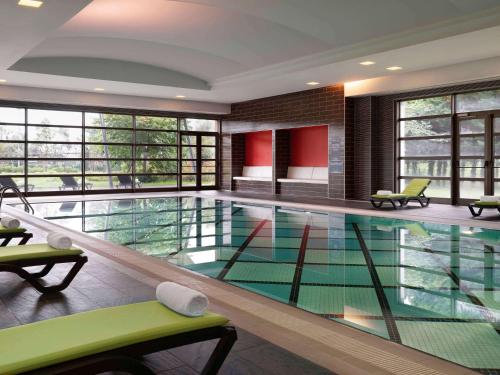 a large swimming pool with green chairs and windows at Novotel Trabzon in Trabzon