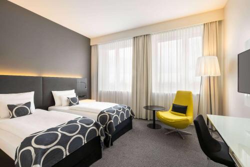 um quarto de hotel com duas camas e uma cadeira amarela em Vienna House by Wyndham Andel's Berlin em Berlim