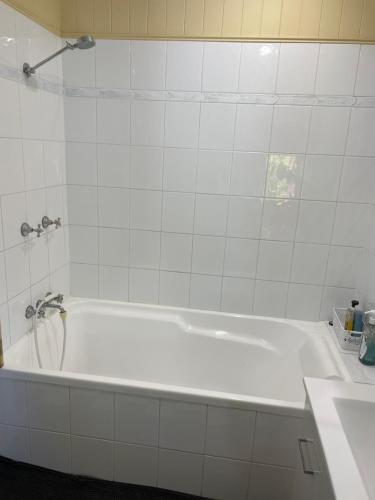 a white bath tub in a white tiled bathroom at Beautiful house with city views in Brisbane