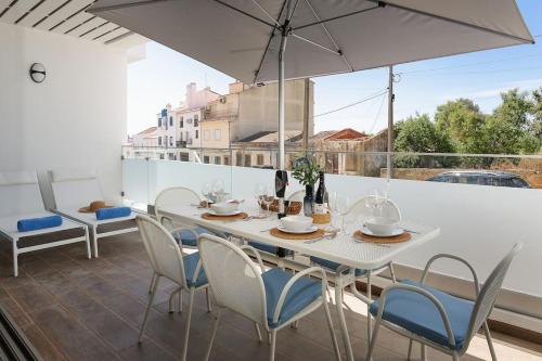 a white table with chairs and an umbrella on a balcony at Dália modern apartment Five minutes to beach in Luz