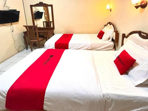 two beds in a hotel room with red and white blankets at RedDoorz at Hotel Madani Syariah Lempuyangan in Demangan