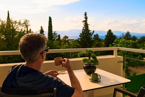 a man sitting at a table with a cup of coffee at Malinska Green Apartments in Malinska
