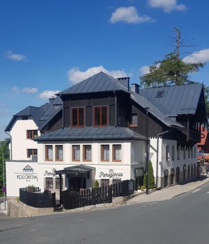 ein weißes Gebäude mit schwarzem Dach an einer Straße in der Unterkunft Hotel Kolorowa in Karpacz