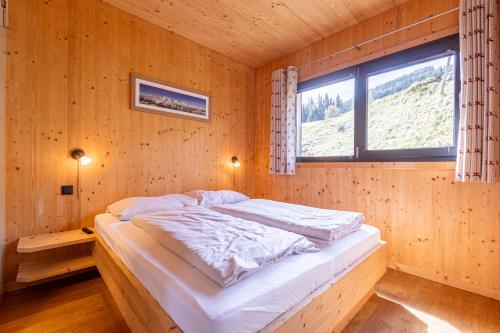 a bed in a wooden room with a window at Alpenchalets Reiteralm by ALPS RESORTS in Schladming