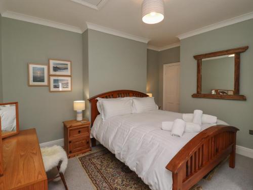 a bedroom with a bed with white sheets and a mirror at Five Bells Cottage in Alnmouth