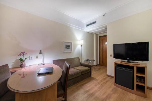 uma sala de estar com um sofá, uma mesa e uma televisão em Hotel Cassino Tower Campinas Cambuí em Campinas