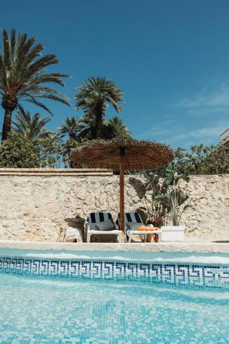 a pool with chairs and an umbrella and palm trees at Los Bungalows Del Arenal in Jávea