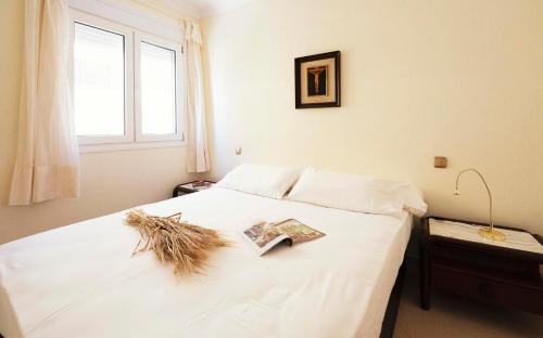 a bedroom with a white bed with a book on it at Summerlandrota La Caleta in Rota