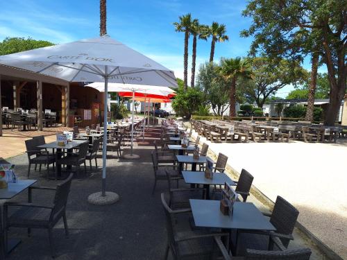 une rangée de tables et de chaises avec un parasol dans l'établissement Chez Cédric et Vivi mobil home 6 pers, à Argelès-sur-Mer