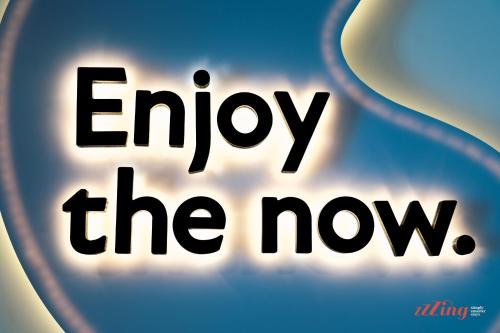 a sign with the words enjoy the now at Stuart Rooms by Zzzing in Il-Gżira