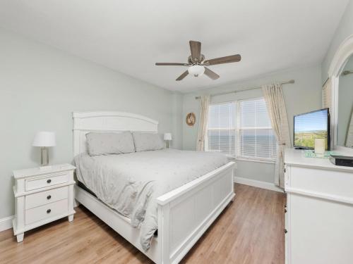 a white bedroom with a bed and a ceiling fan at Sea Winds 501 - Corner Breeze in Ormond Beach