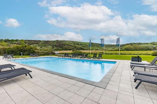 a large swimming pool with benches and tables and a field at Fletcher Zuiderduin Beachhotel in Westkapelle