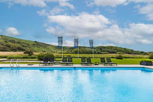 a large swimming pool with chairs and a hill at Fletcher Zuiderduin Beachhotel in Westkapelle