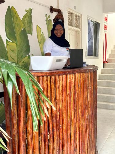 a woman standing behind a wooden counter with a laptop at POLE POLE House in Nungwi