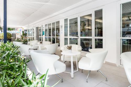 un restaurante con sillas blancas, mesas y plantas en Hotel Vibra Vila, en Ibiza