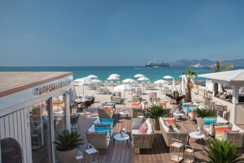 eine Terrasse mit Liegestühlen und Sonnenschirmen am Strand in der Unterkunft Hotel Croisette Beach Cannes - Mgallery in Cannes