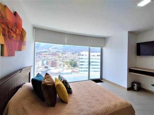 um quarto com uma cama com almofadas e uma grande janela em Suite Piso #20 Con Vista Al Pichincha em Quito