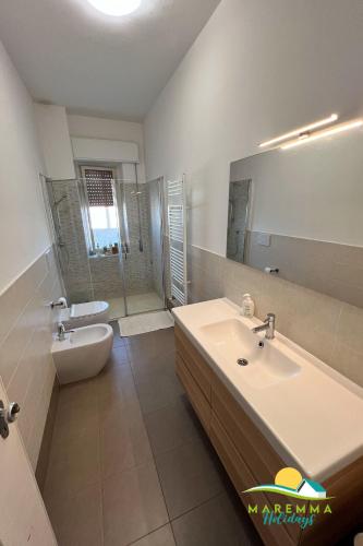 a bathroom with a sink and a toilet and a mirror at Maremma Holidays-Gardenia Apartment in Follonica