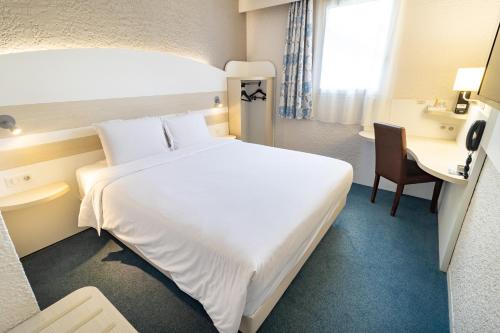 Habitación de hotel con cama blanca grande y escritorio. en Kyriad Auxerre Appoigny, en Appoigny