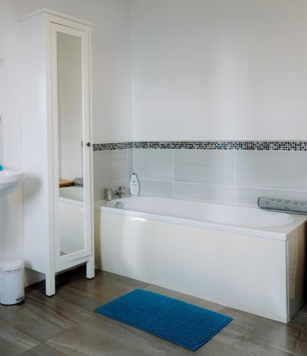 a white bathroom with a tub and a blue rug at Stable Cottage - Kinbane Self Catering Cottages in Ballintoy