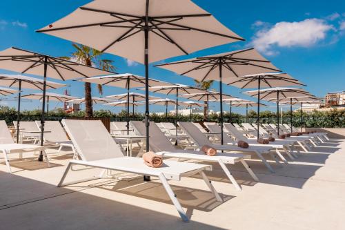 a row of white lounge chairs and umbrellas at The Londoner Hotel St. Julian's in St Julian's