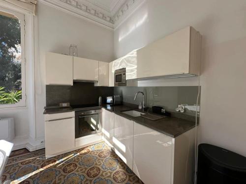 une cuisine avec des armoires blanches, un évier et une fenêtre dans l'établissement C025 Villa Toscane Bel Appartement Bourgeois, à Cannes