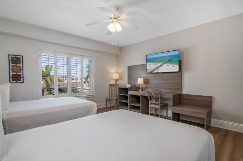 a bedroom with two beds and a desk and a tv at Naples Park Central Hotel in Naples