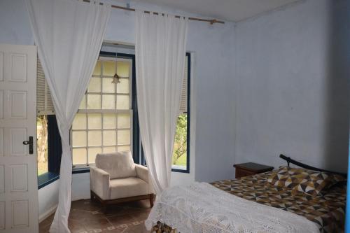 a bedroom with a bed and a chair and a window at Lindo sitio com piscina em Rio Novo-Minas Gerais in Rio Novo