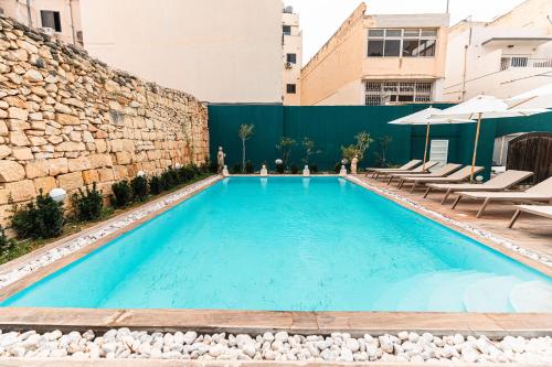a swimming pool with chairs and a stone wall at Suite 1 at Palazzo Seraphim Boutique living in St Julians in St. Julianʼs
