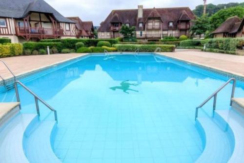 une grande piscine bleue avec des maisons en arrière-plan dans l'établissement Le sublime Olivier Normand, 3P cosy et luxe avec jardin, piscine & tennis, vélos, à Deauville