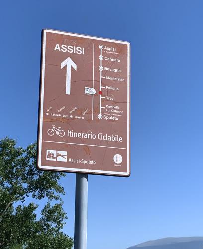 a brown sign on a pole with trees in the background at A 2 Passi Appartamento in Foligno